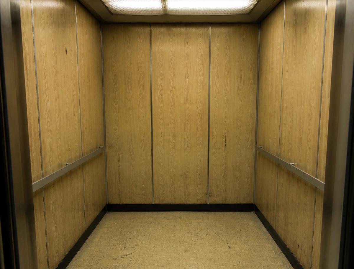 Cabine de elevador antiga com revestimento desgastado antes da reforma